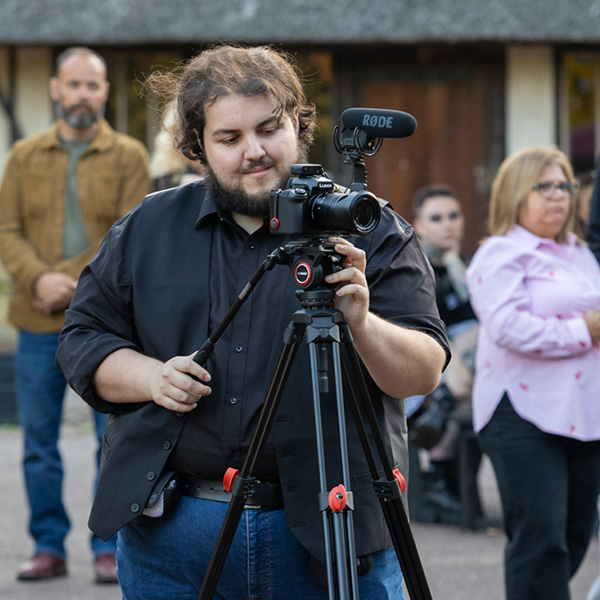Tom stood with a video camera and microphone on a tripod.